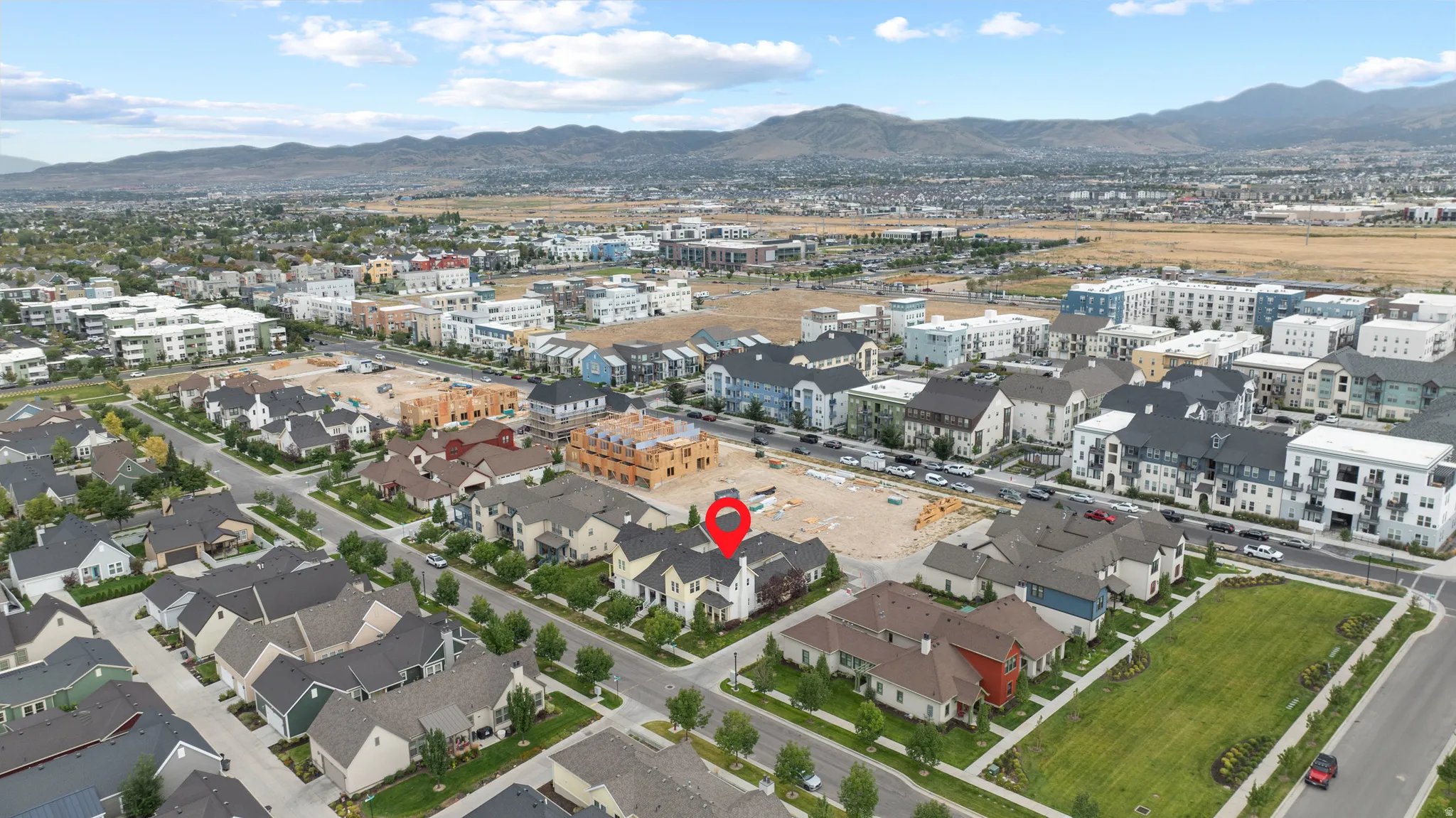 Aerial view showcasing a community of single-family homes and multi-story residential buildings, set against a backdrop of distant mountains
