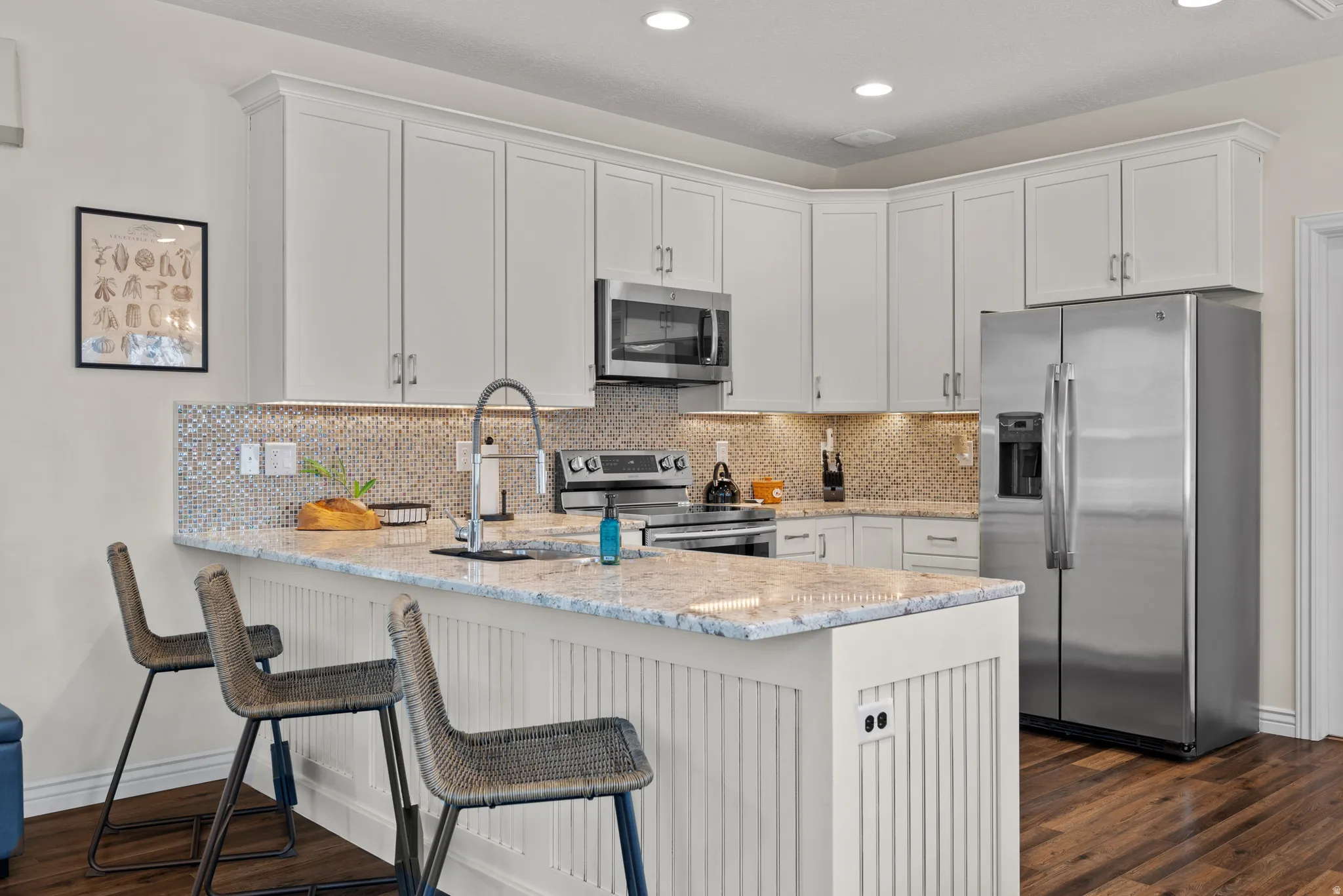 Kitchen featuring white shaker cabinetry, stainless steel appliances, a mosaic tile backsplash, and a large central island with a light-toned countertop and beadboard paneling