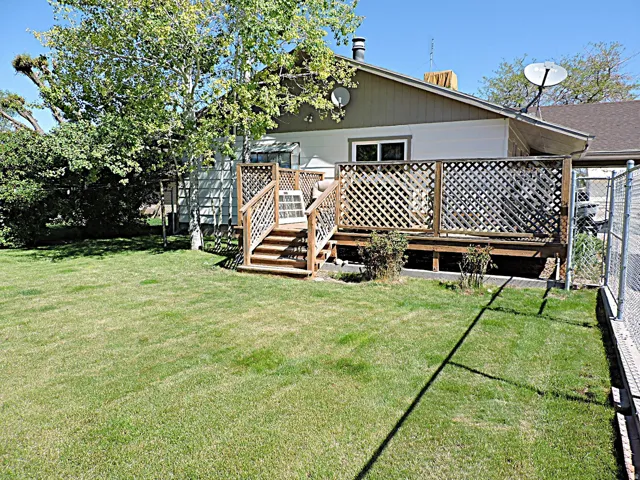 Rear exterior with a wooden deck featuring lattice railing, stairs, and a level lawn