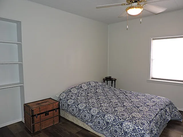 Bedroom featuring a built-in shelving unit, wood-finish flooring, and a ceiling fan with integrated lighting