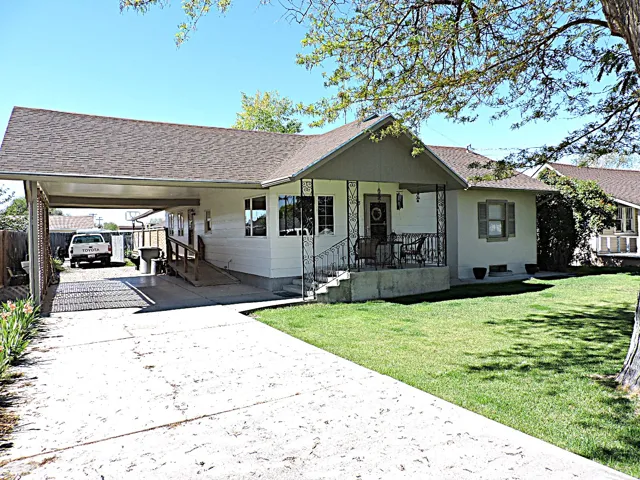 Single-story residence featuring a covered front porch with decorative railing, a concrete driveway, an attached carport, and a wooden accessibility ramp
