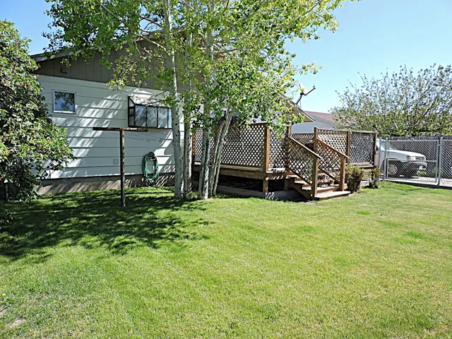 Rear exterior featuring a wooden deck with lattice railing, stairs, and a level lawn area