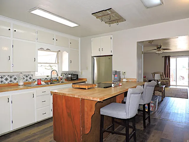Kitchen featuring white cabinetry, butcher block countertops, patterned backsplash, wood-finish flooring, and a stainless steel refrigerator