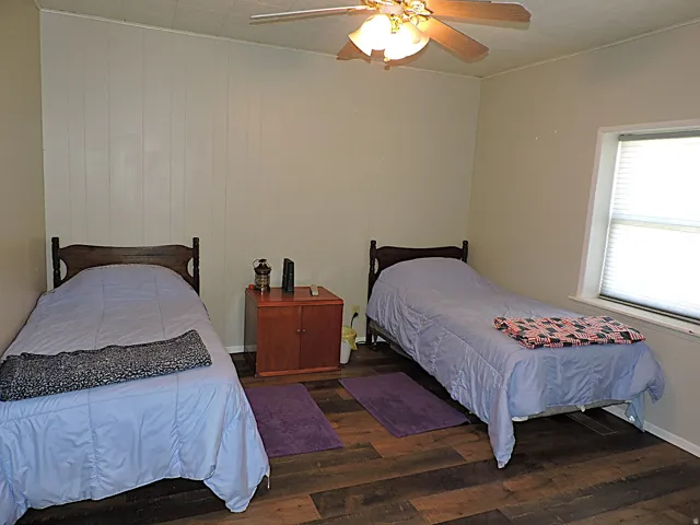 Room featuring wood-finish flooring, white paneled wall accents, and a ceiling fan with integrated lighting