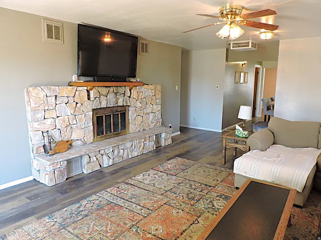 Stone-faced fireplace with hearth seating, wood-finish flooring, and ceiling fan with integrated lighting
