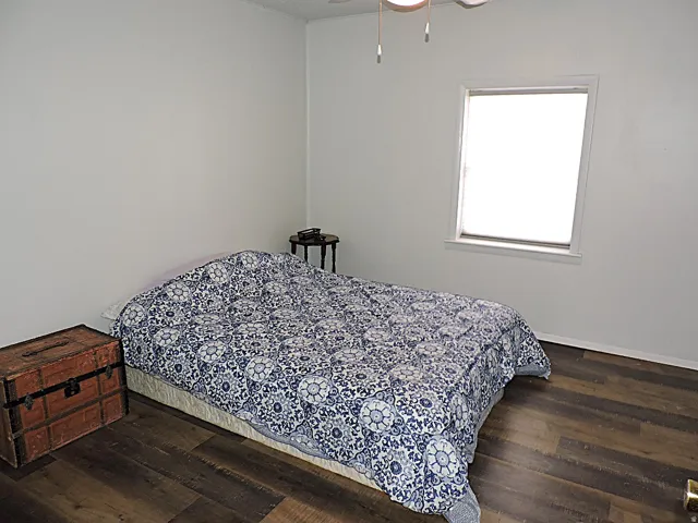 Room featuring wood-finish flooring, a ceiling fan with integrated lighting, and a single window with a white frame