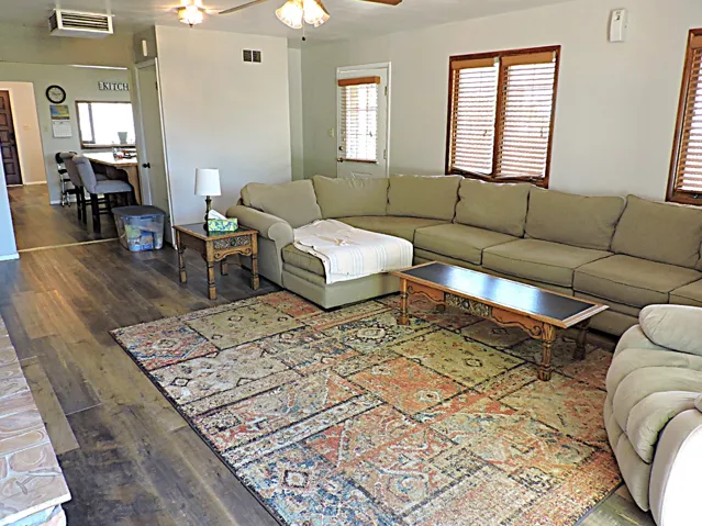 Spacious living area featuring wood-finish flooring, white walls, and a ceiling fan with integrated lighting