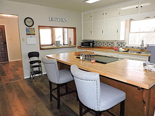 Kitchen featuring wood-finish flooring, an island with a built-in cooktop and light wood countertop, white cabinetry, and a patterned tile backsplash