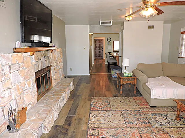 Living area featuring a stone fireplace with hearth, wood-finish flooring, and a ceiling fan with integrated lighting