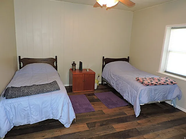Room featuring wood-finish flooring, a ceiling fan with integrated lighting, and a white paneled accent wall
