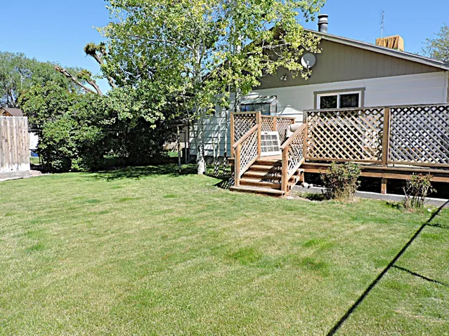 Spacious grassy yard featuring a wood deck with lattice privacy screening