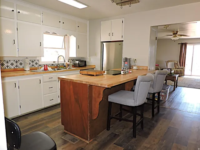 Kitchen featuring wood-finish flooring, white cabinetry, a patterned backsplash, wood-finish countertops, and a stainless steel refrigerator
