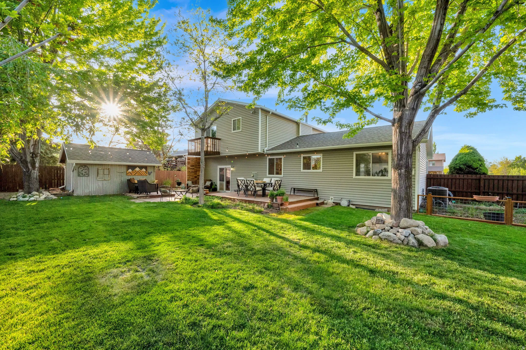 Expansive backyard featuring a lush lawn, a multi-level deck, a detached shed, a second-story balcony, and mature trees