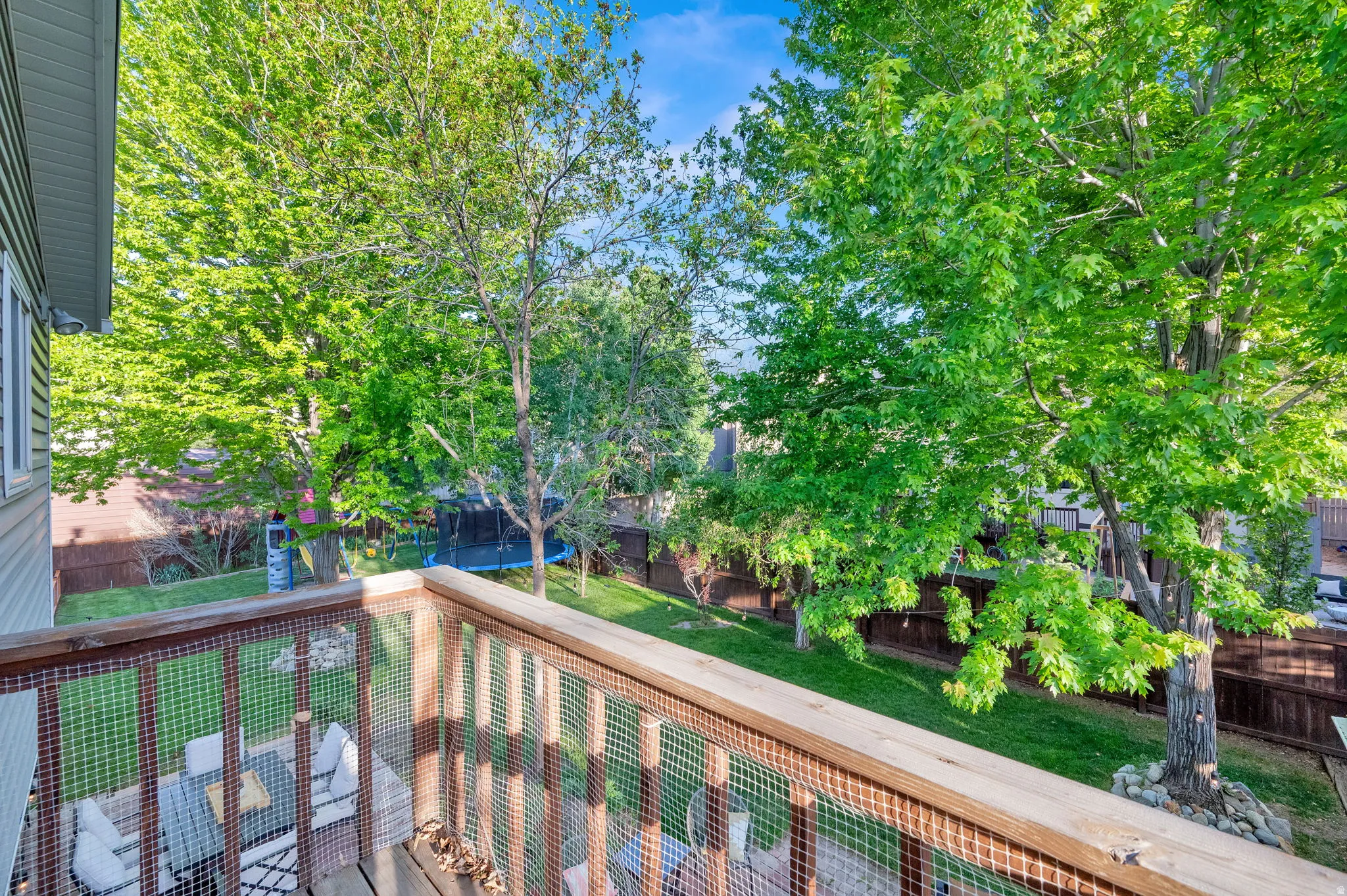 Elevated wood deck with a slatted railing and wire mesh infill, overlooking a lush green yard with mature trees