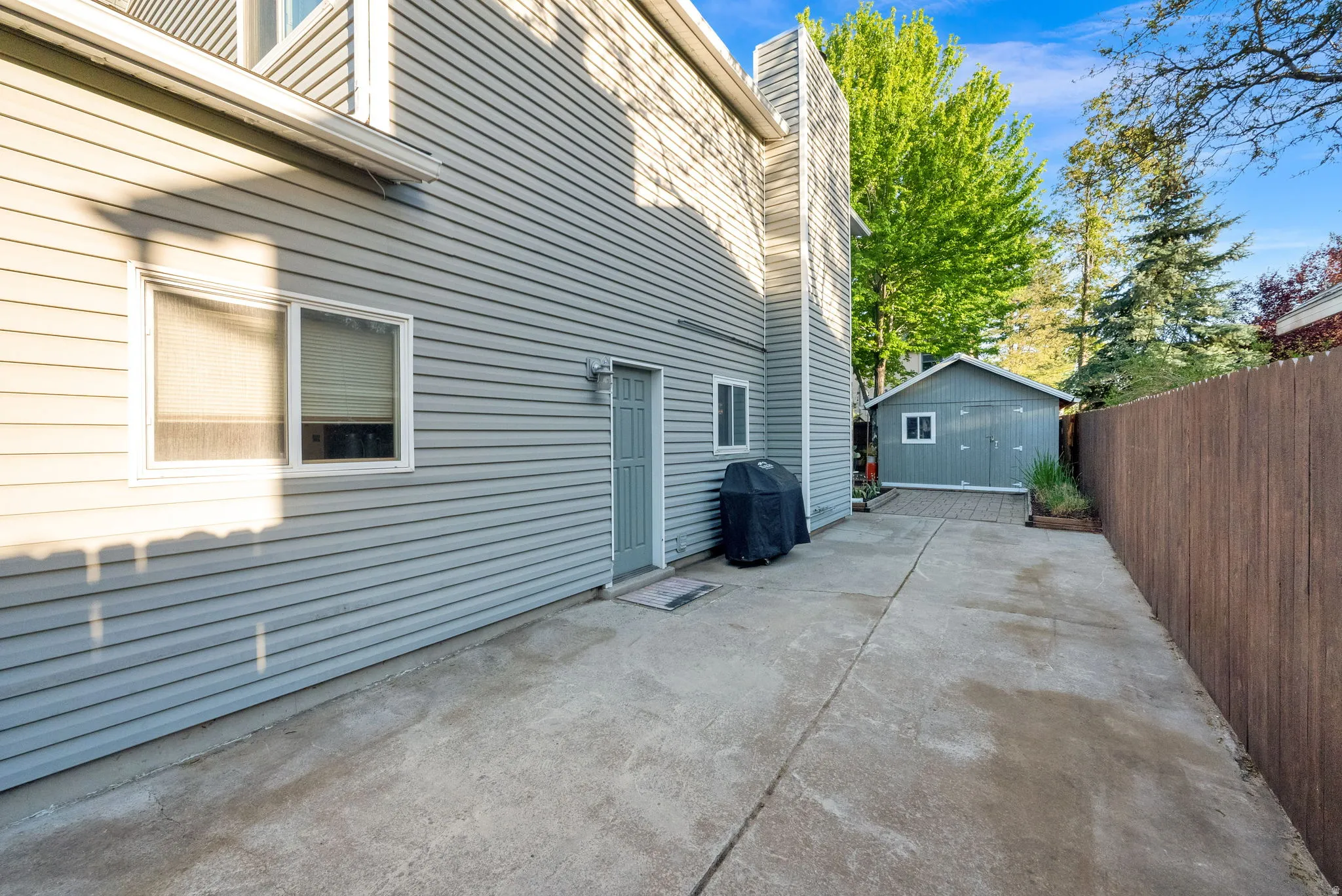 Concrete patio area featuring a detached storage shed, privacy fencing, and exterior siding