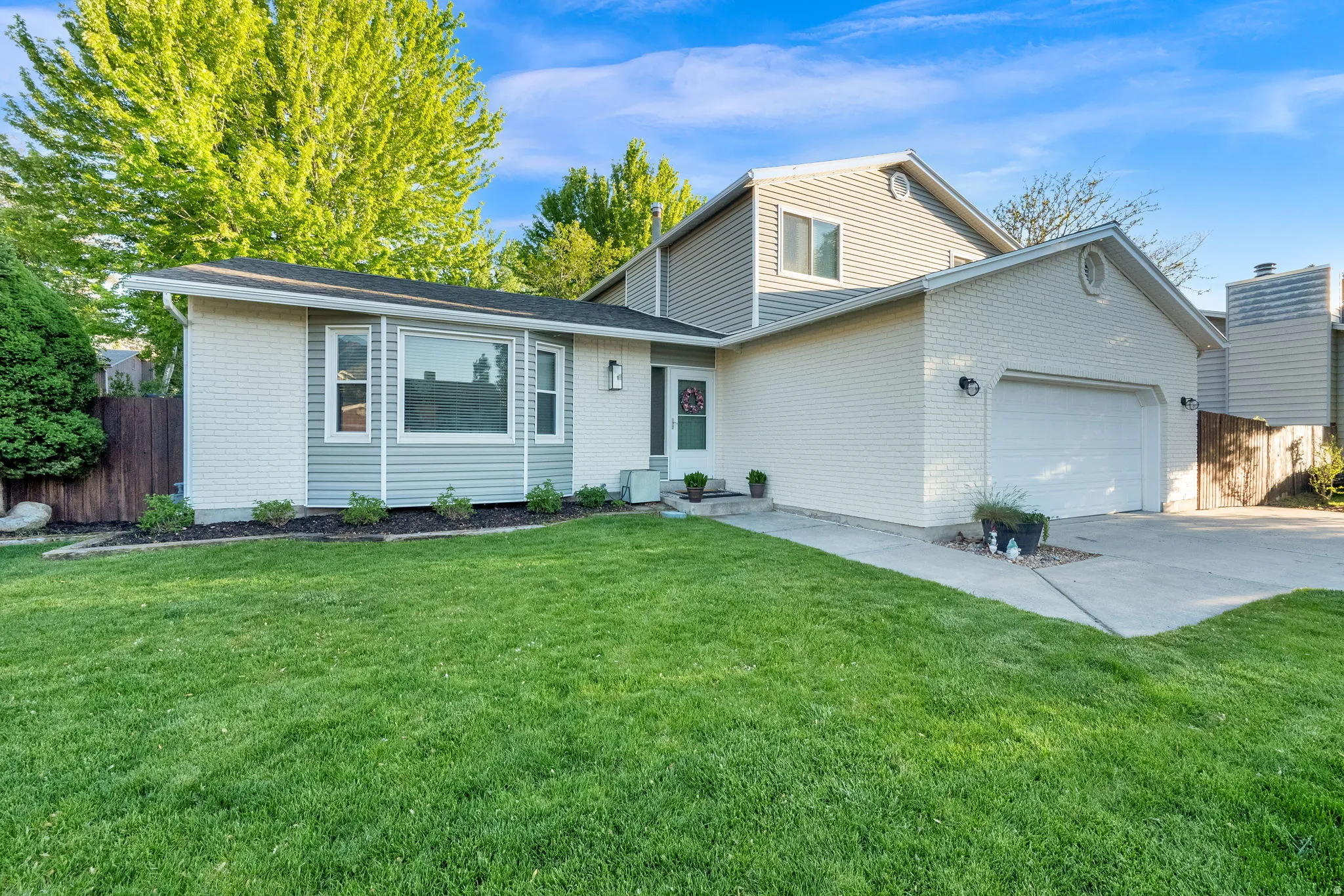 Exterior featuring light brick and horizontal siding, a two-car garage, a well-maintained lawn, established landscaping, and a concrete driveway