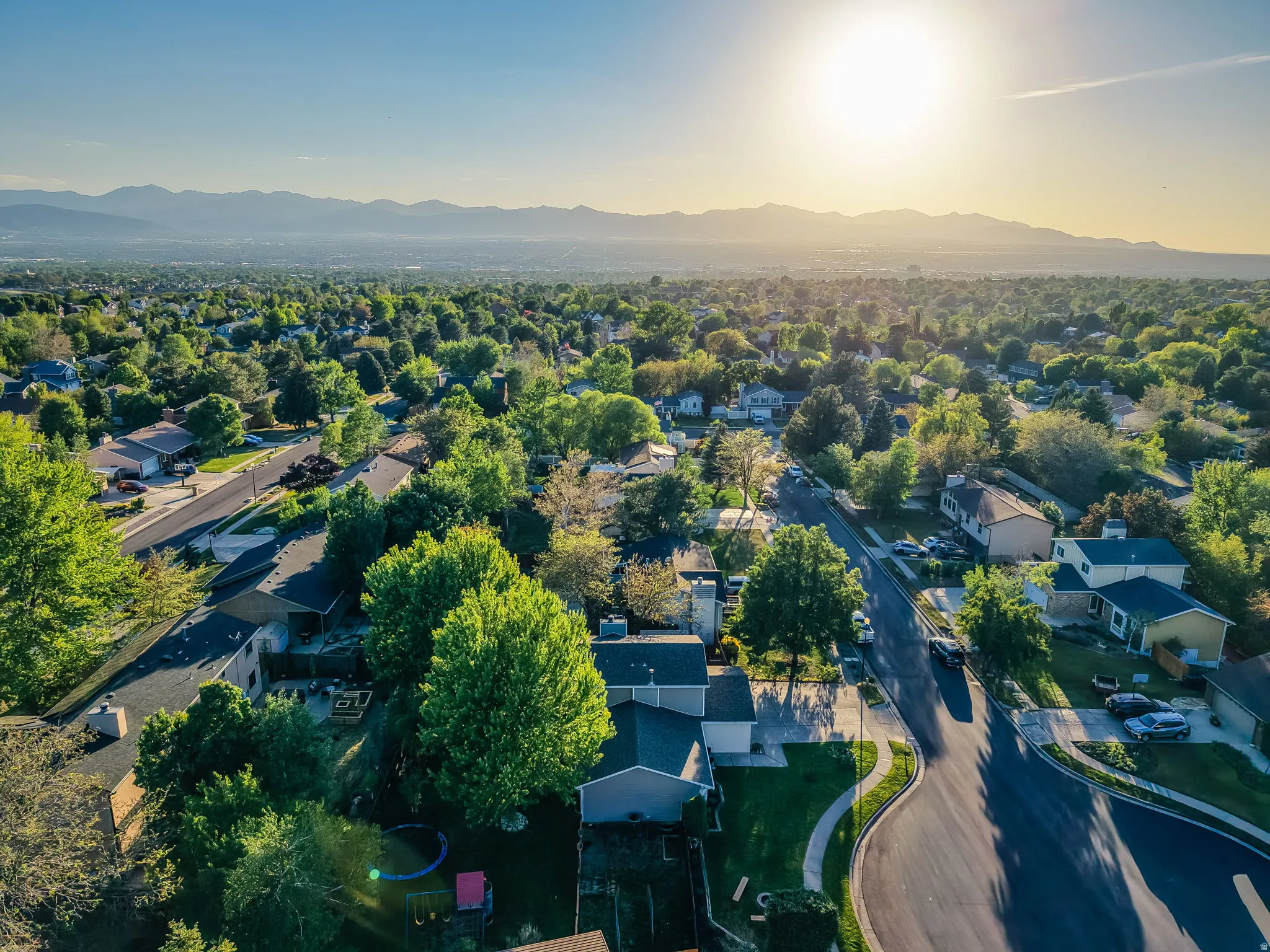 Expansive aerial perspective showcasing a residential area with mature tree canopies and mountain scenery