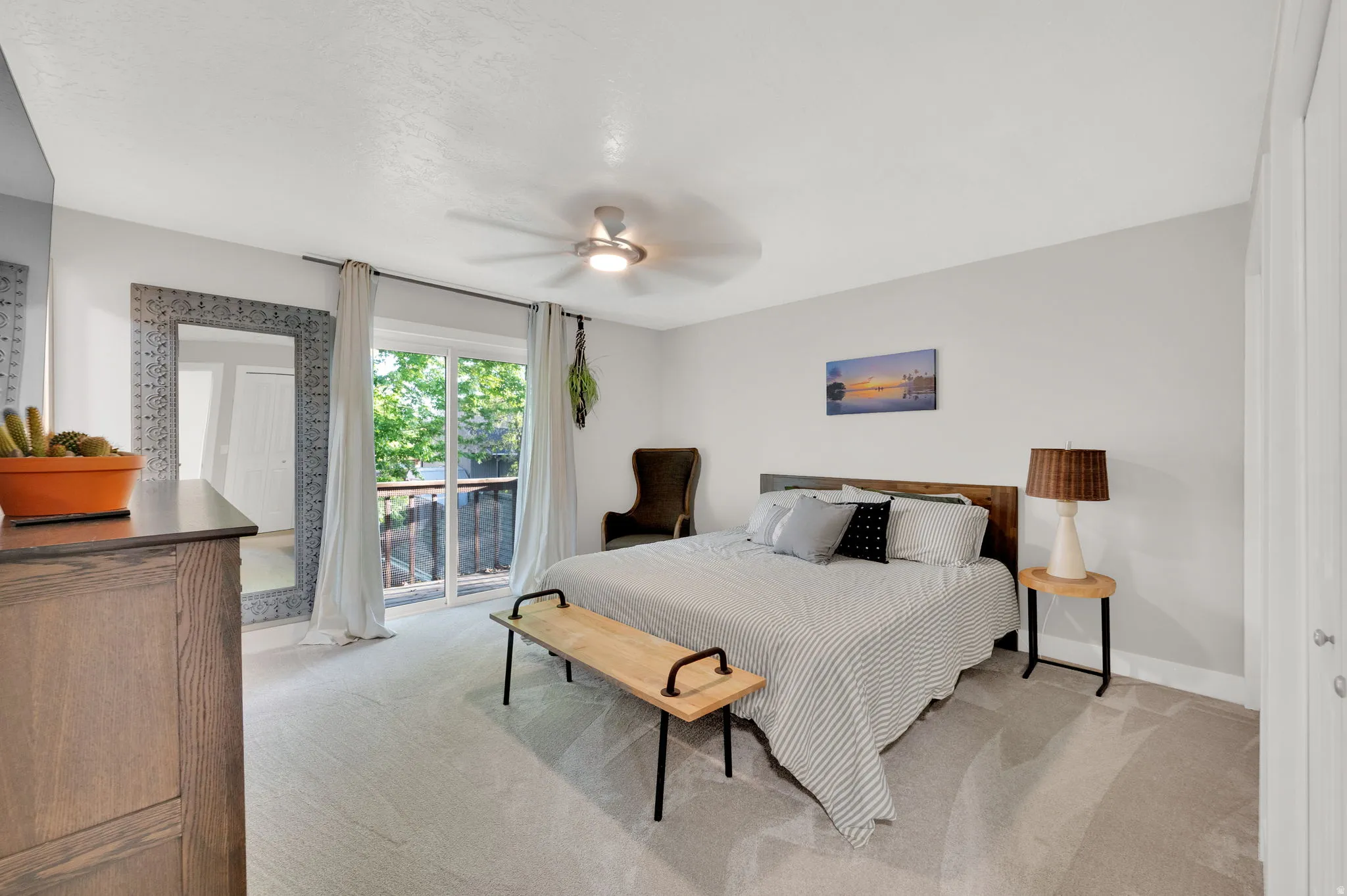 Carpeted room featuring a ceiling fan, sliding glass doors to an outdoor area, wood-finish headboard, and white paneled closet doors