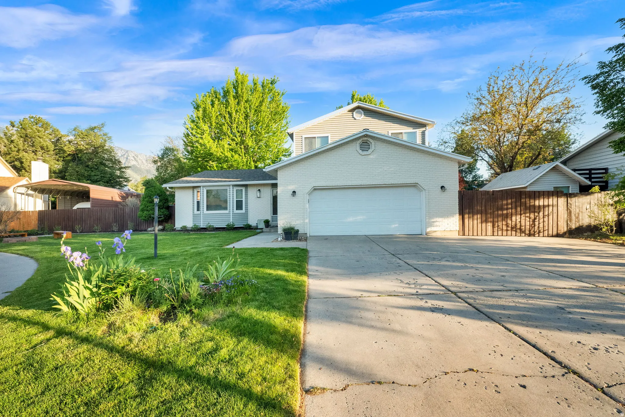 Two-story residence featuring a two-car garage, concrete driveway, and a manicured lawn with mature landscaping