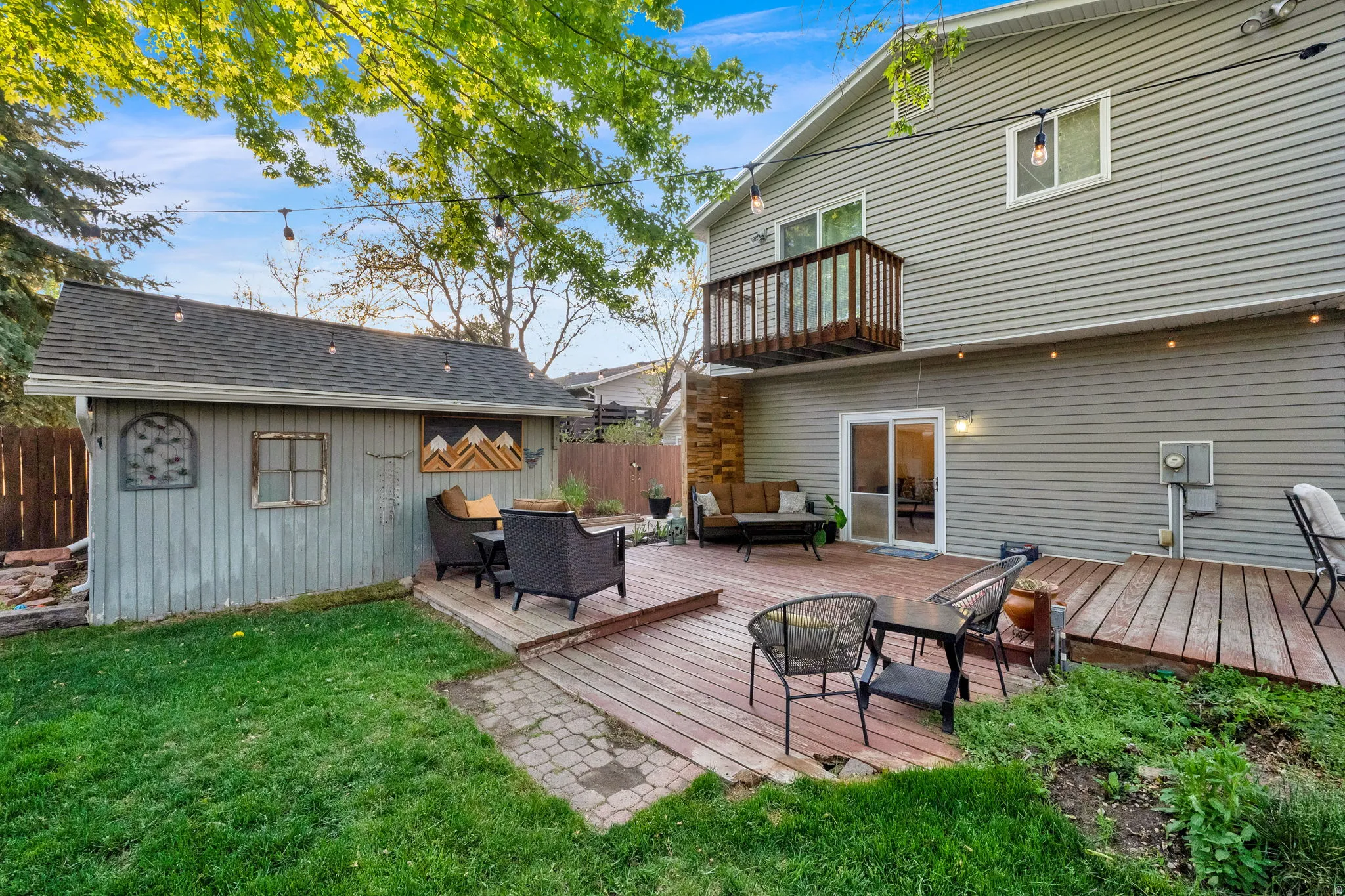Expansive backyard featuring a multi-level wood deck, a manicured lawn, a detached storage shed with a shingle roof, and a second-story wood balcony