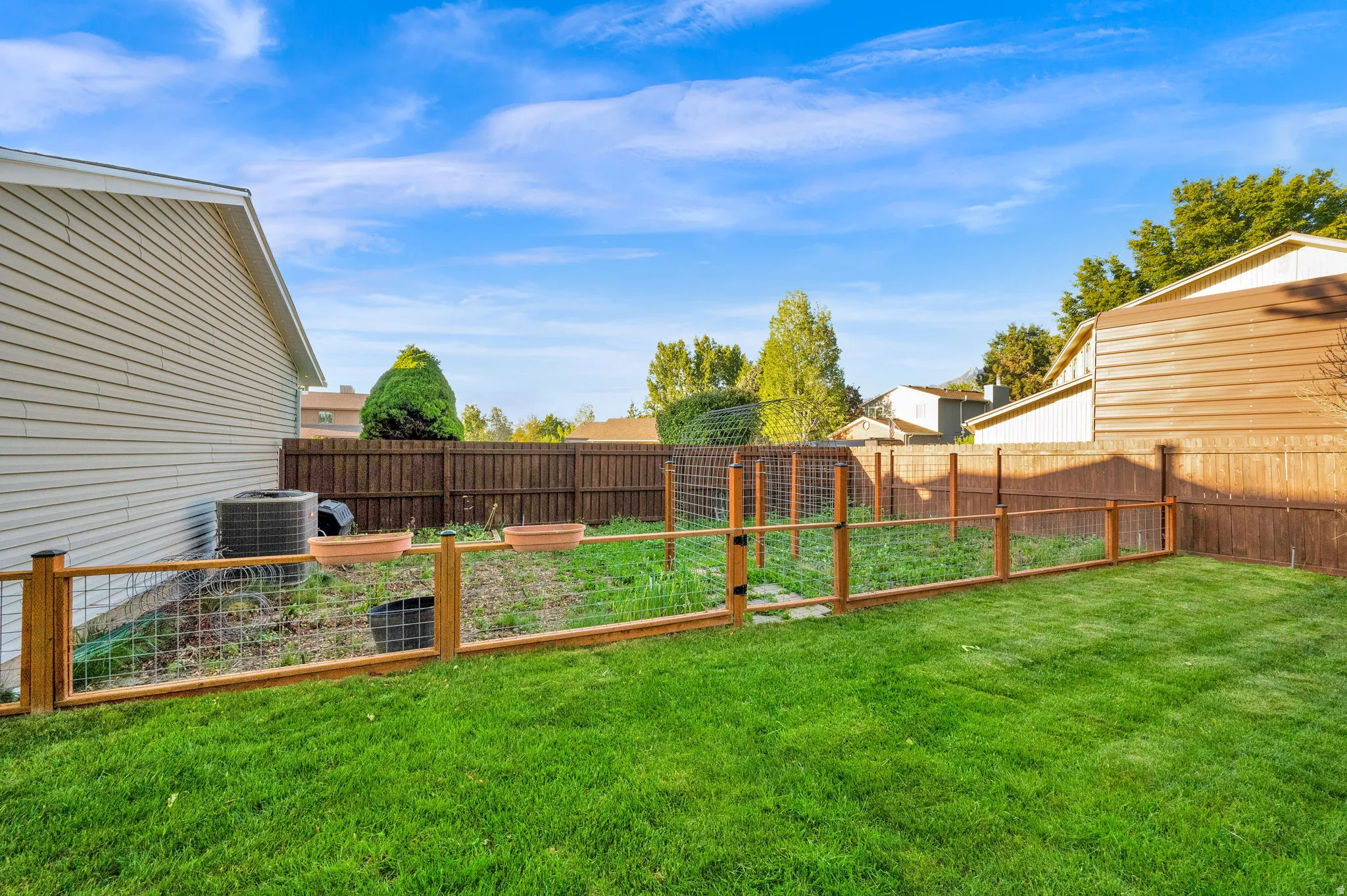 Expansive backyard featuring a lush lawn, wood fencing, and a dedicated garden area with wire fencing