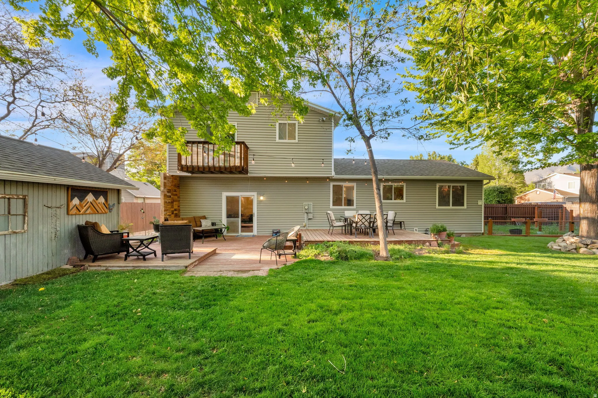 Spacious rear yard with a green lawn, two-story siding exterior, ground-level deck, upper-level balcony, and a detached shed