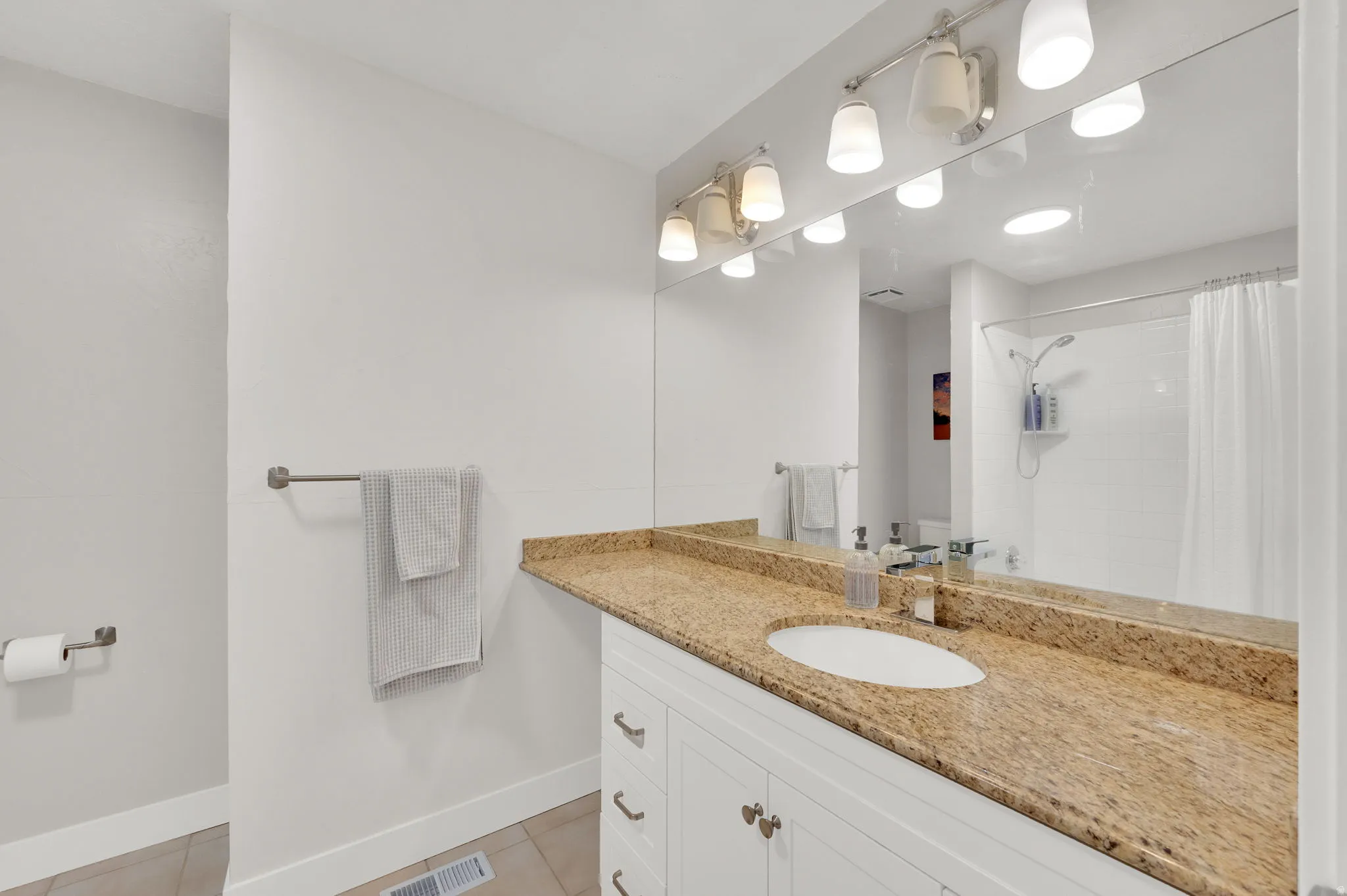 Bathroom vanity featuring a light-toned granite countertop, undermount sink, and white cabinetry with brushed nickel hardware
