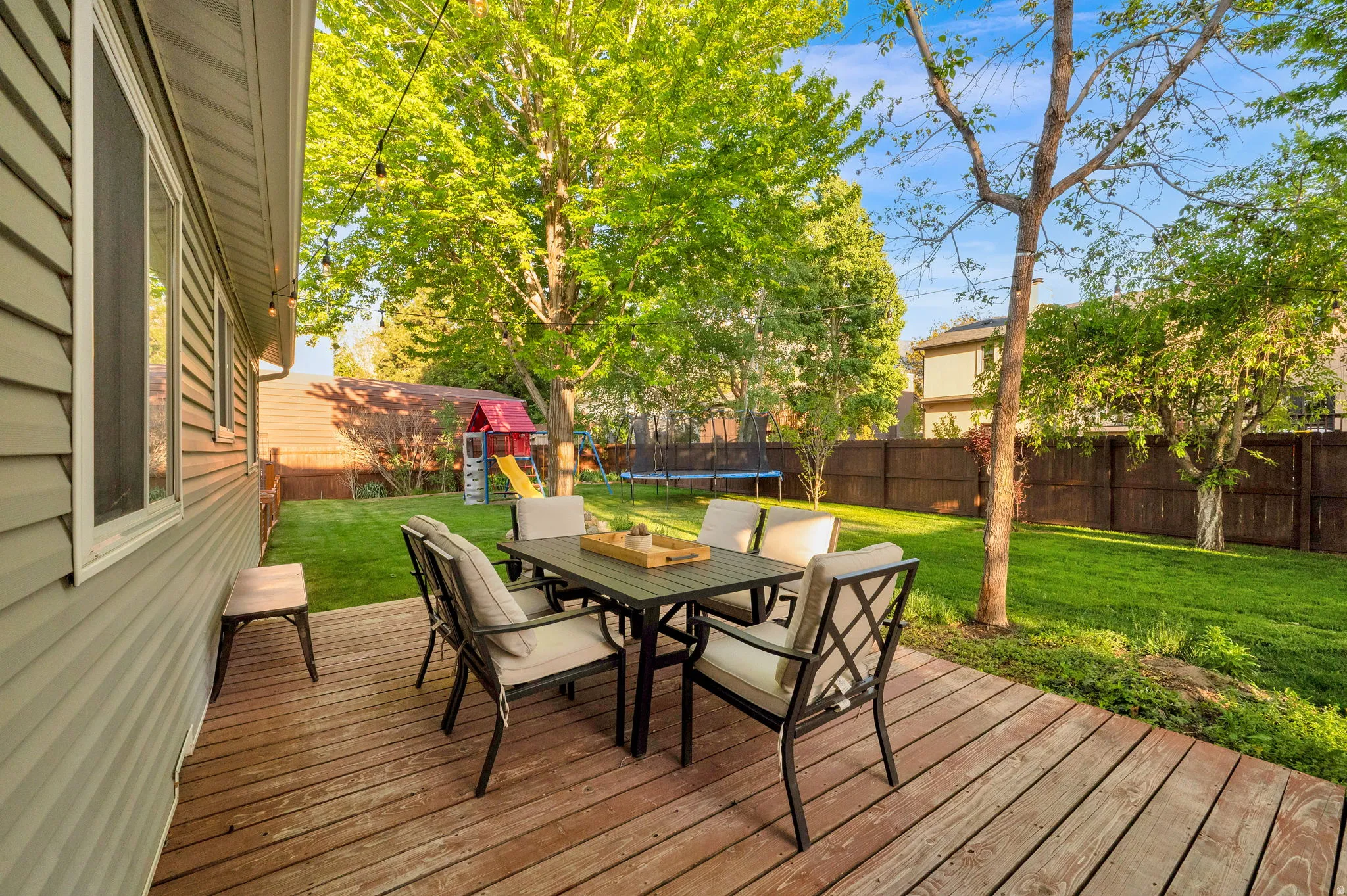 Expansive backyard featuring a wood deck, manicured lawn, and mature trees