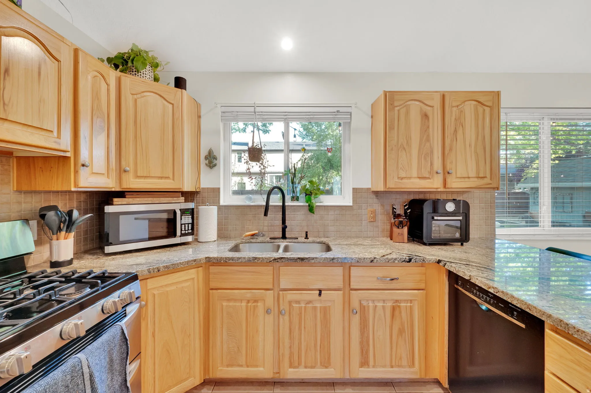 Kitchen featuring light wood cabinetry, a double basin stainless steel sink with a matte black faucet, and patterned stone countertops