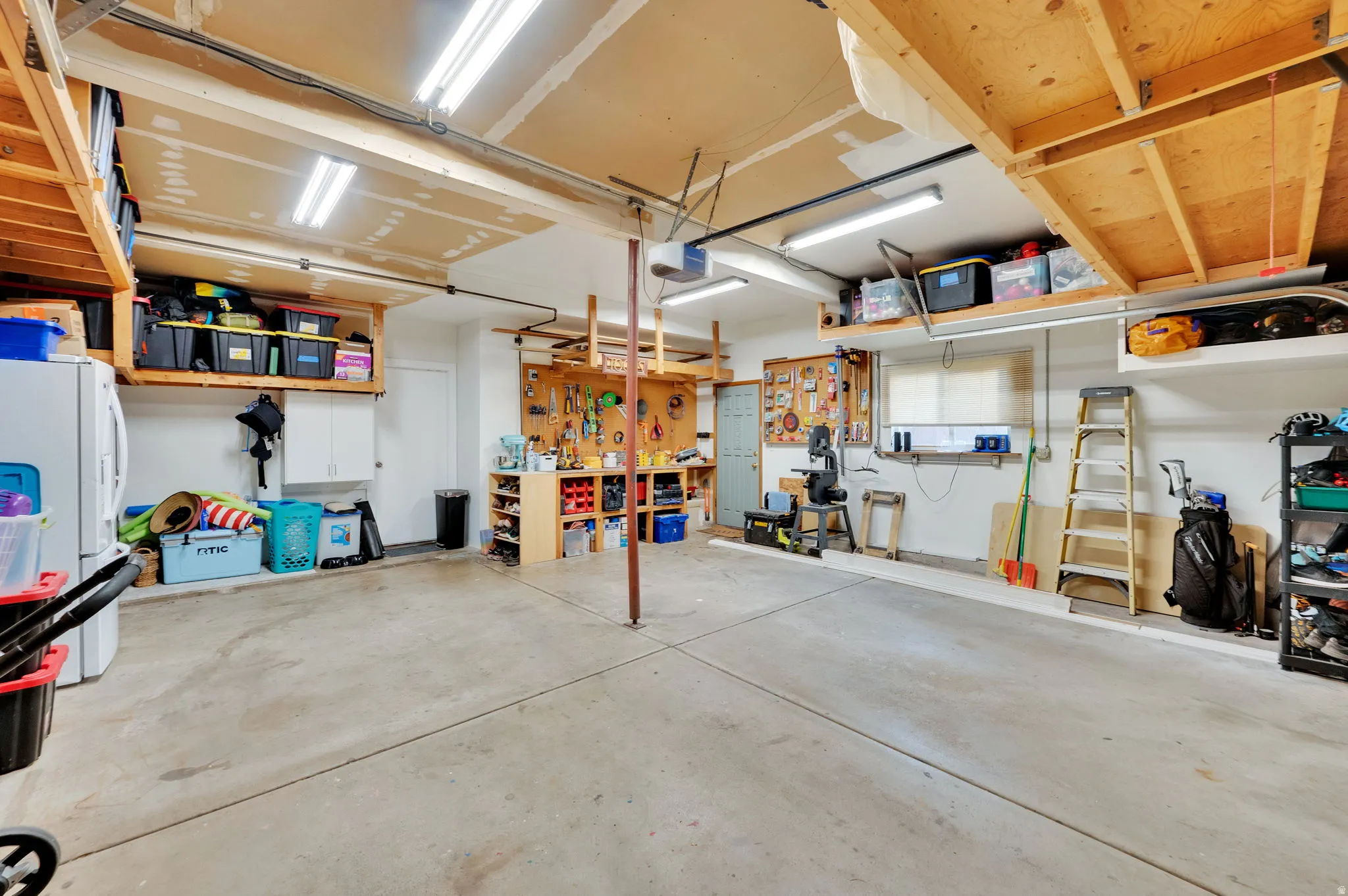 Spacious garage featuring a concrete floor, overhead fluorescent lighting, built-in shelving, a workbench area, and a window