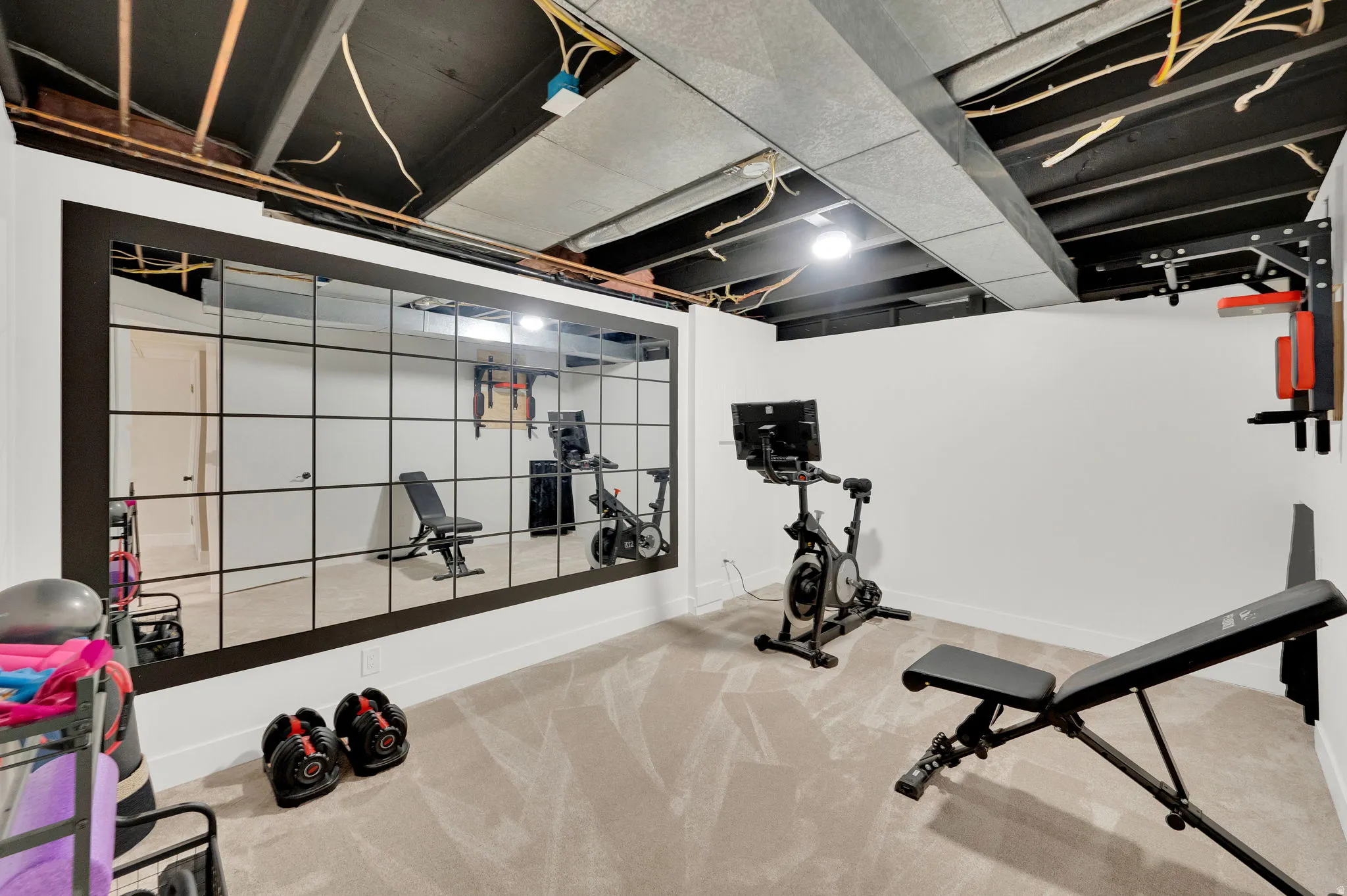 Expansive mirrored wall enhancing a versatile space with neutral carpeting, recessed lighting, and a white baseboard trim
