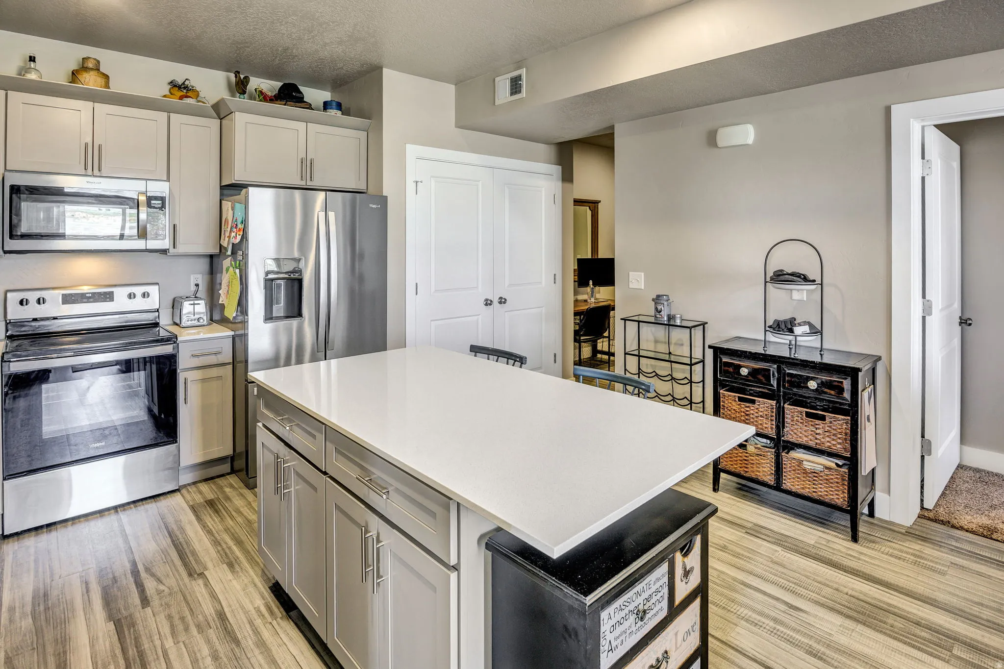 Modern kitchen featuring a large central island with a light-toned countertop, stainless steel appliances, neutral cabinetry, and wood-finish flooring