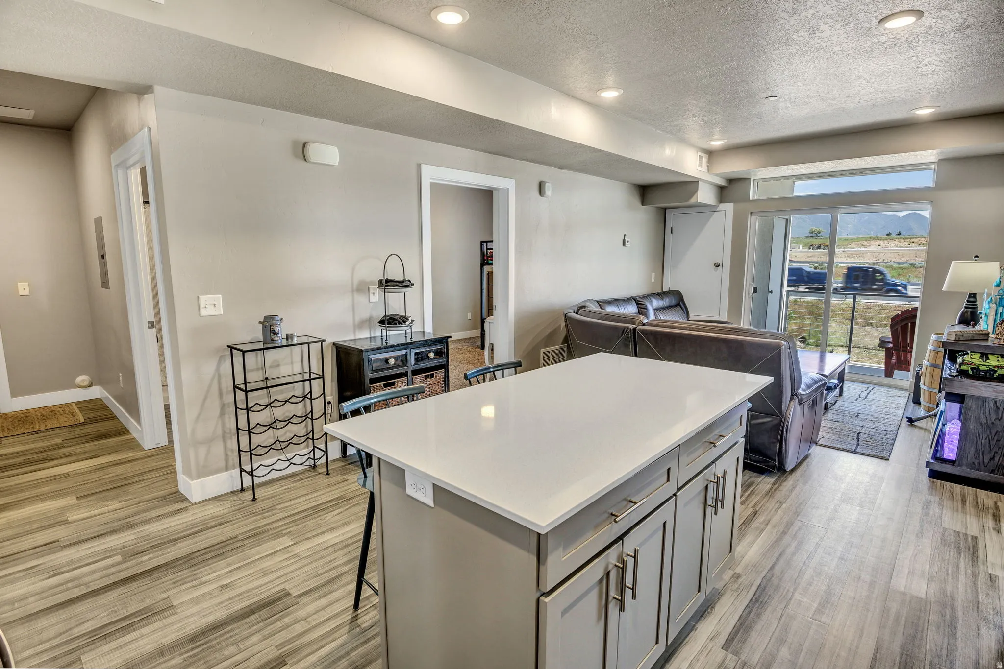 Central kitchen island with a light-toned countertop, wood-finish flooring, recessed lighting, neutral wall paint, and sliding glass doors to the exterior