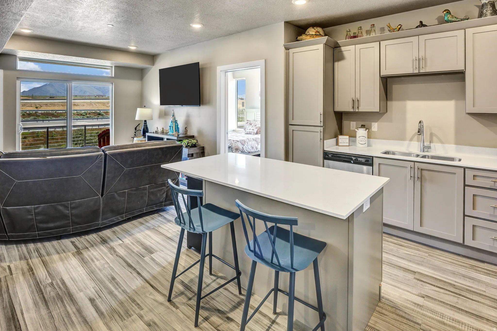 Open-concept living area featuring a kitchen island with seating, wood-finish flooring, recessed lighting, and a sliding glass door