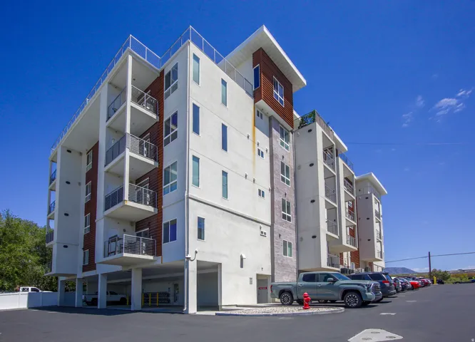 Contemporary multifamily building featuring a white stucco exterior with wood-finish and stone accents