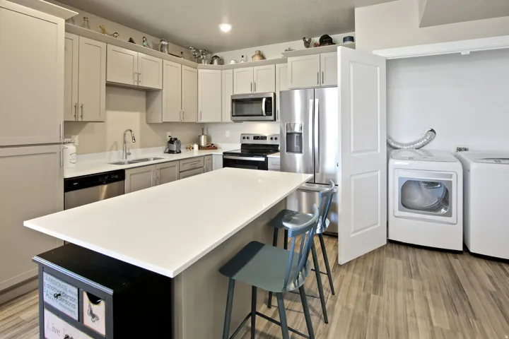 Kitchen featuring an island with white countertop, stainless steel appliances, light-toned cabinetry, and wood-finish flooring