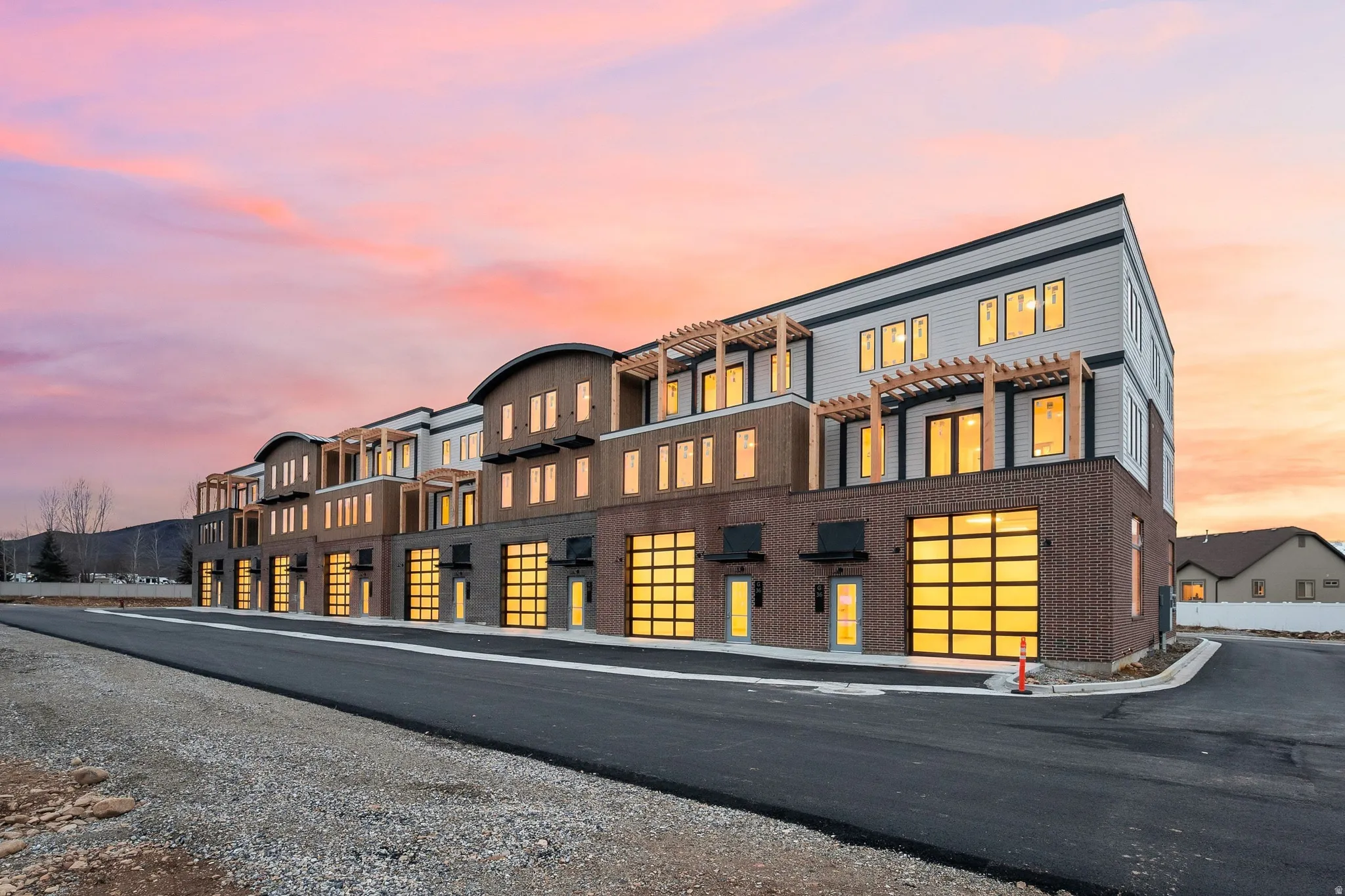 Modern multi-story building featuring brick and siding exterior, large glass panel garage doors, and upper-level balconies with pergolas