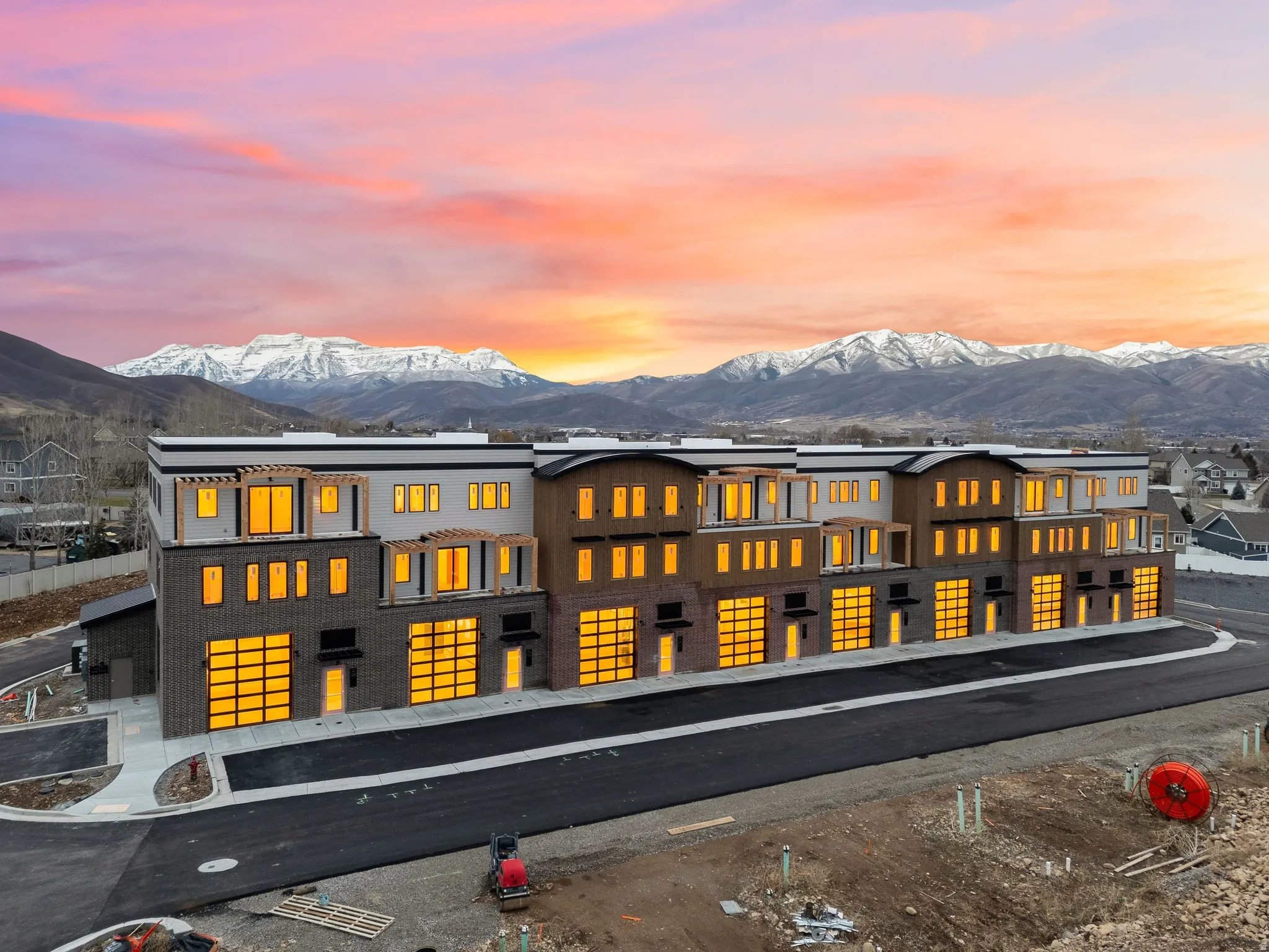 Modern architectural facade with a mix of light-toned and dark-toned siding, integrated garage doors with frosted panels, multiple window configurations, and pergola-style architectural details