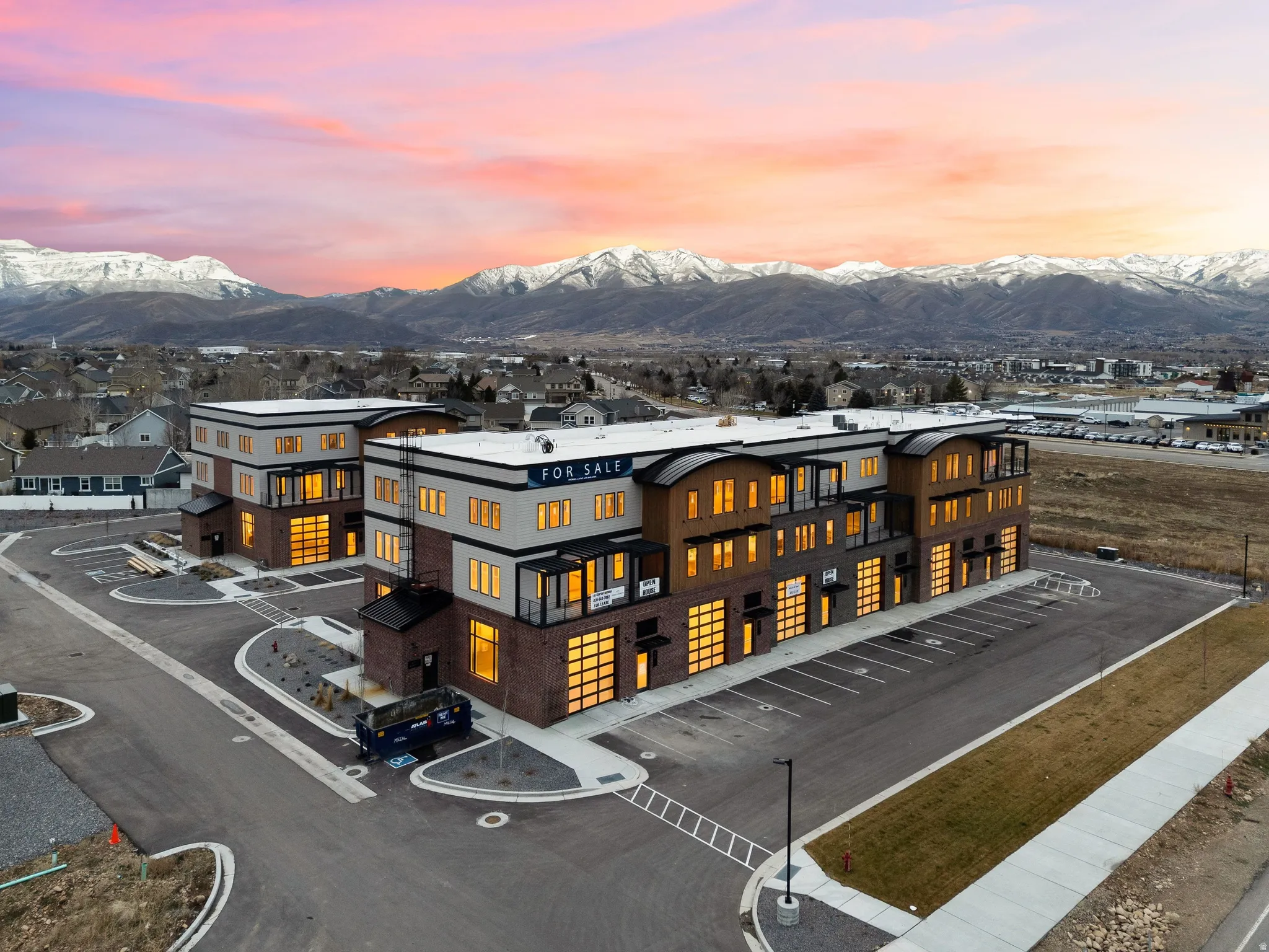 Contemporary multi-level buildings featuring brick and vertical wood-look siding, expansive windows, multiple balconies, and a paved parking area