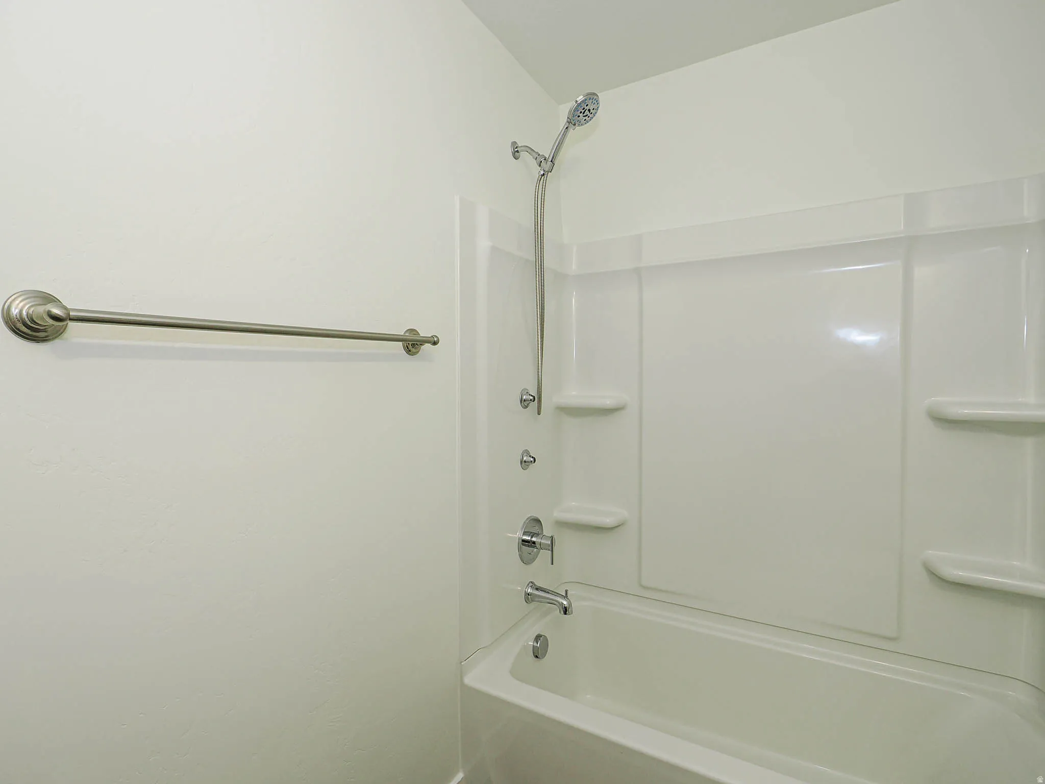 Tub/shower combination featuring a white surround, integrated shelving, and a handheld showerhead