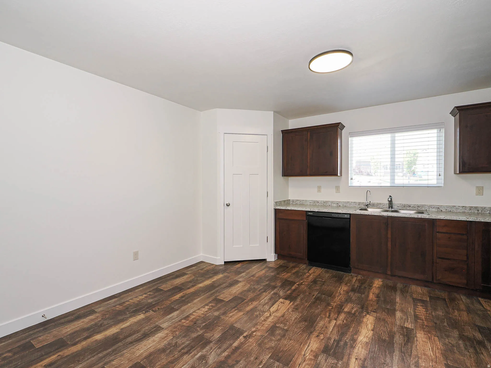 Kitchen area featuring dark wood-finish cabinetry, light-toned countertops, and a stainless steel sink with a single-handle faucet