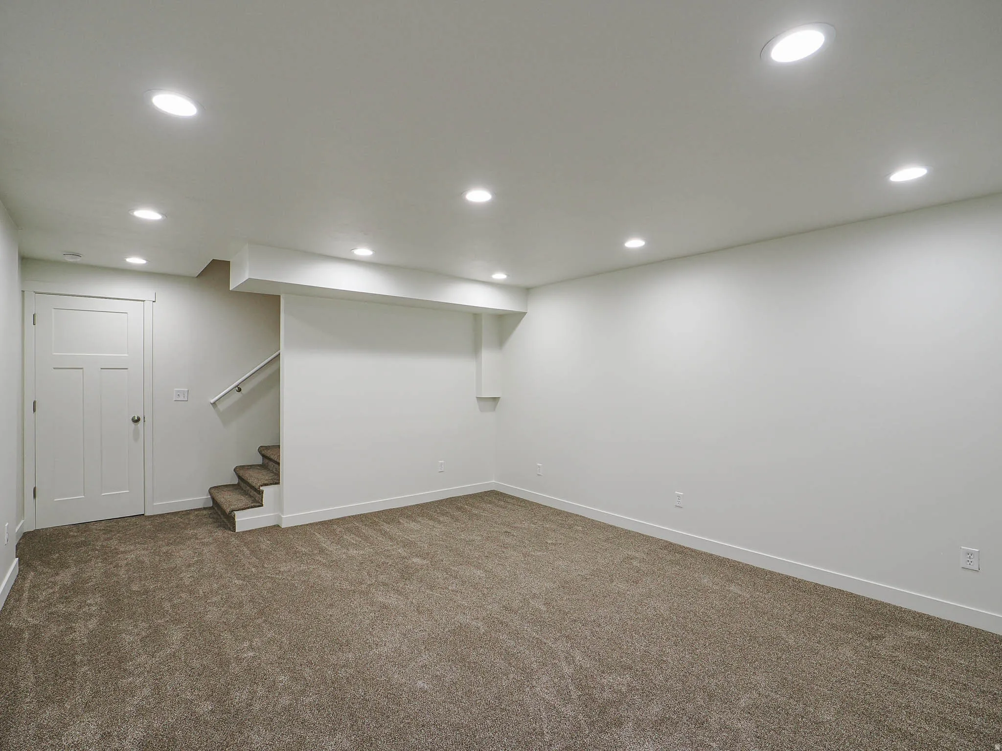 Spacious room featuring neutral carpeting, recessed lighting, white walls, and a staircase with a handrail