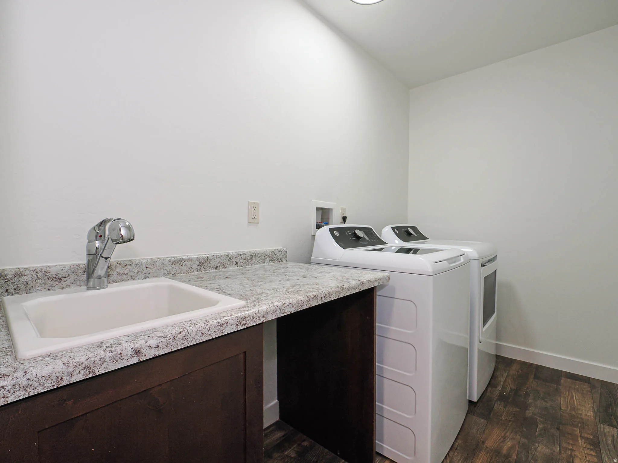 Dedicated utility space featuring a built-in sink with a high-arc faucet, speckled countertop, dark wood-finish cabinetry, and wood-finish flooring