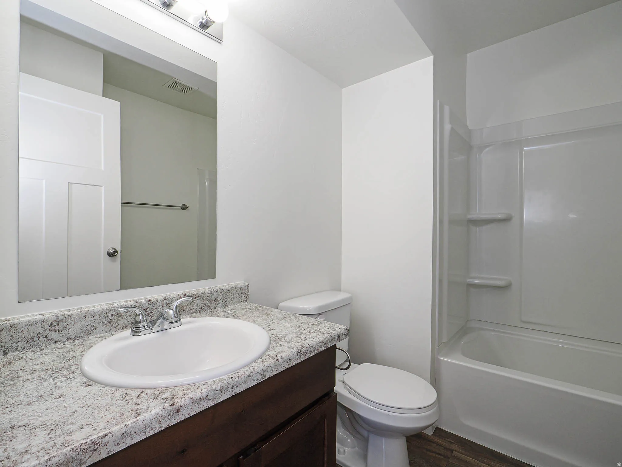 Bathroom featuring a white bathtub and shower combination, wood-finish flooring, and a vanity with a white countertop and integrated sink