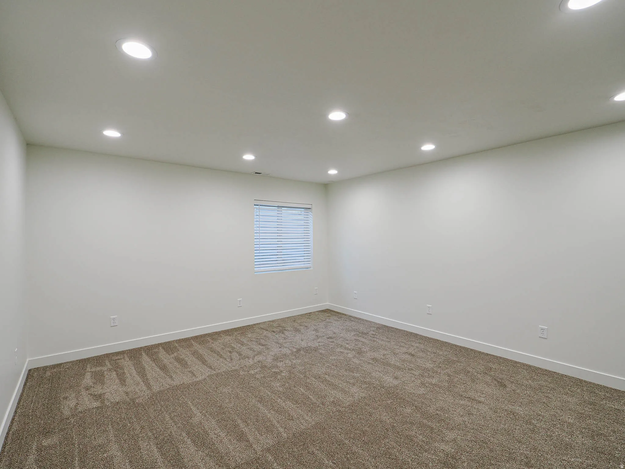 Recessed lighting illuminates this room, featuring light-colored walls, brown patterned carpeting, and a window with horizontal blinds