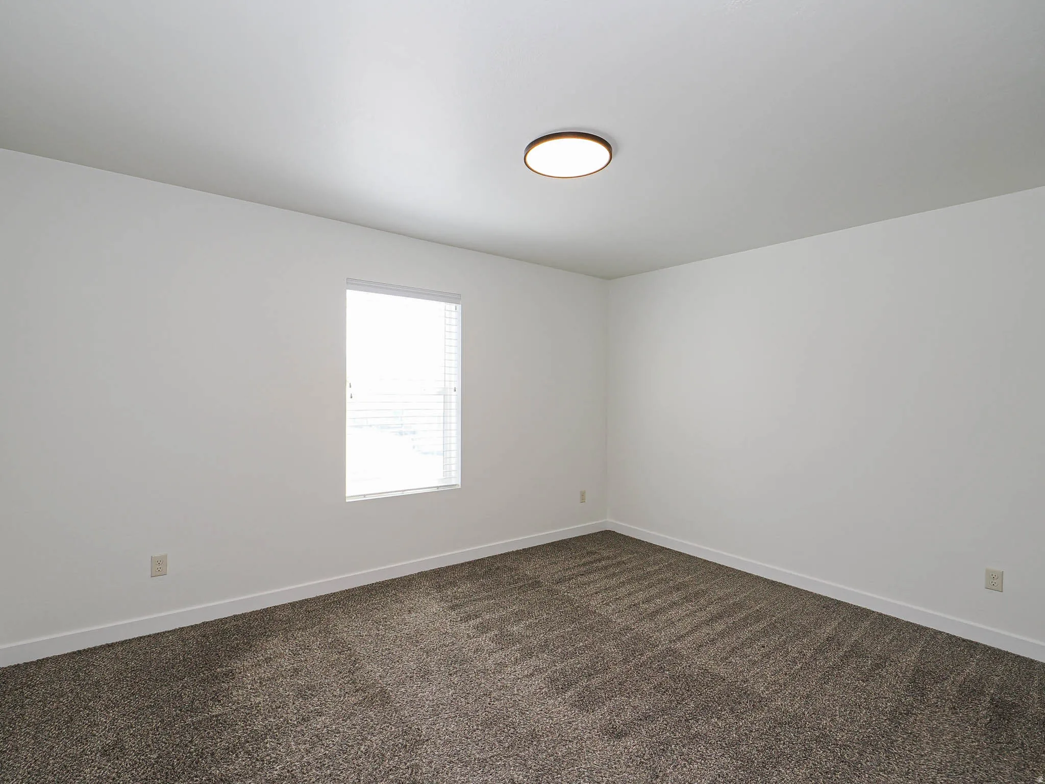 Room featuring neutral white walls, a single window with blinds, and a modern flush-mount ceiling light