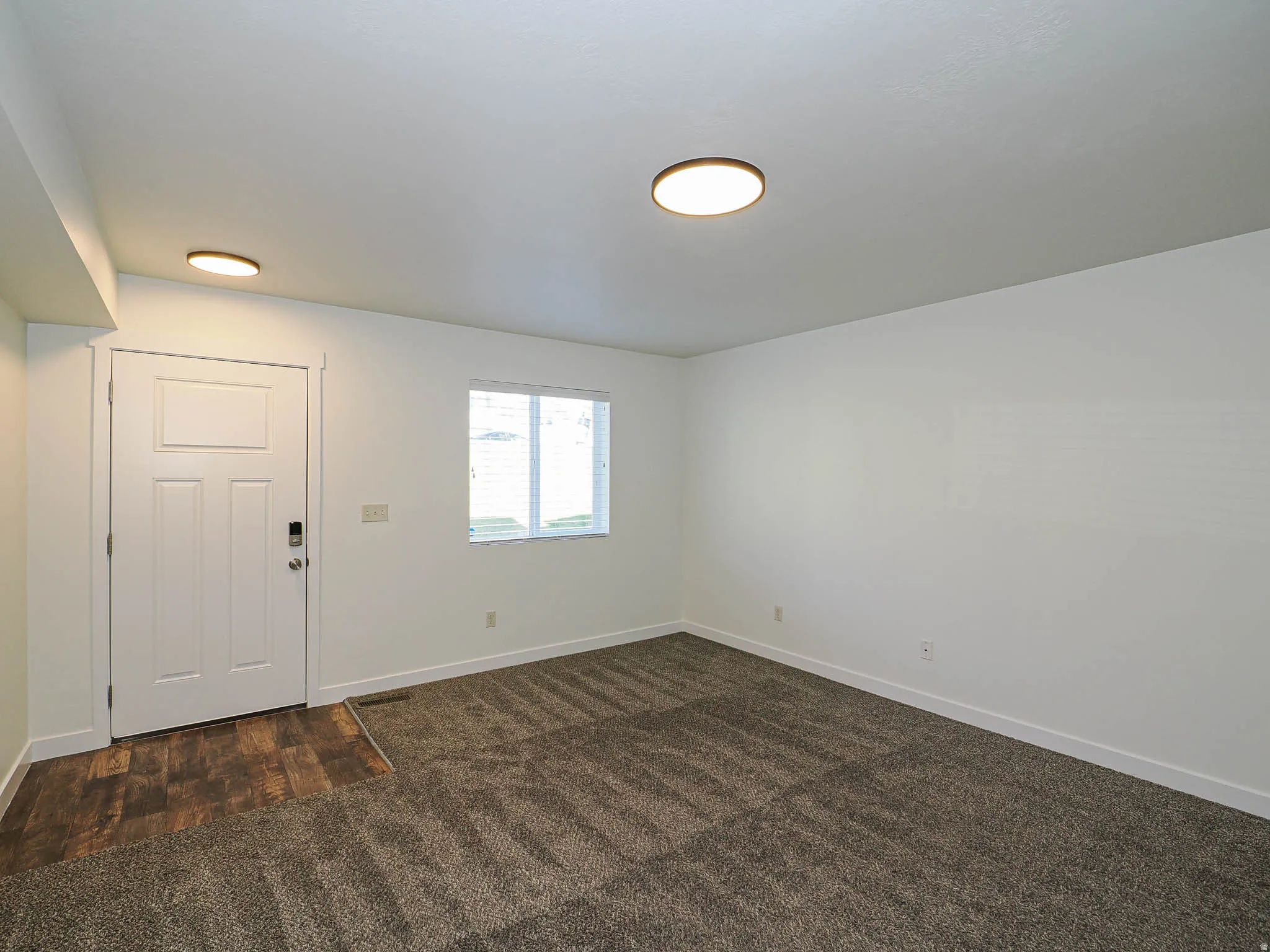Entry area featuring wood-finish flooring, a white paneled door with smart lock, and a window with blinds