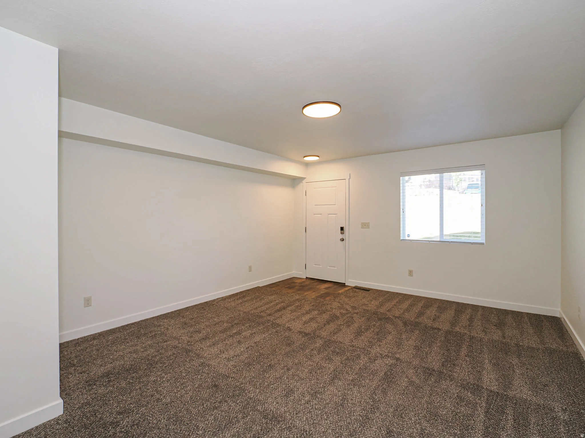 Spacious room featuring neutral carpeting, white walls, and a multi-pane window