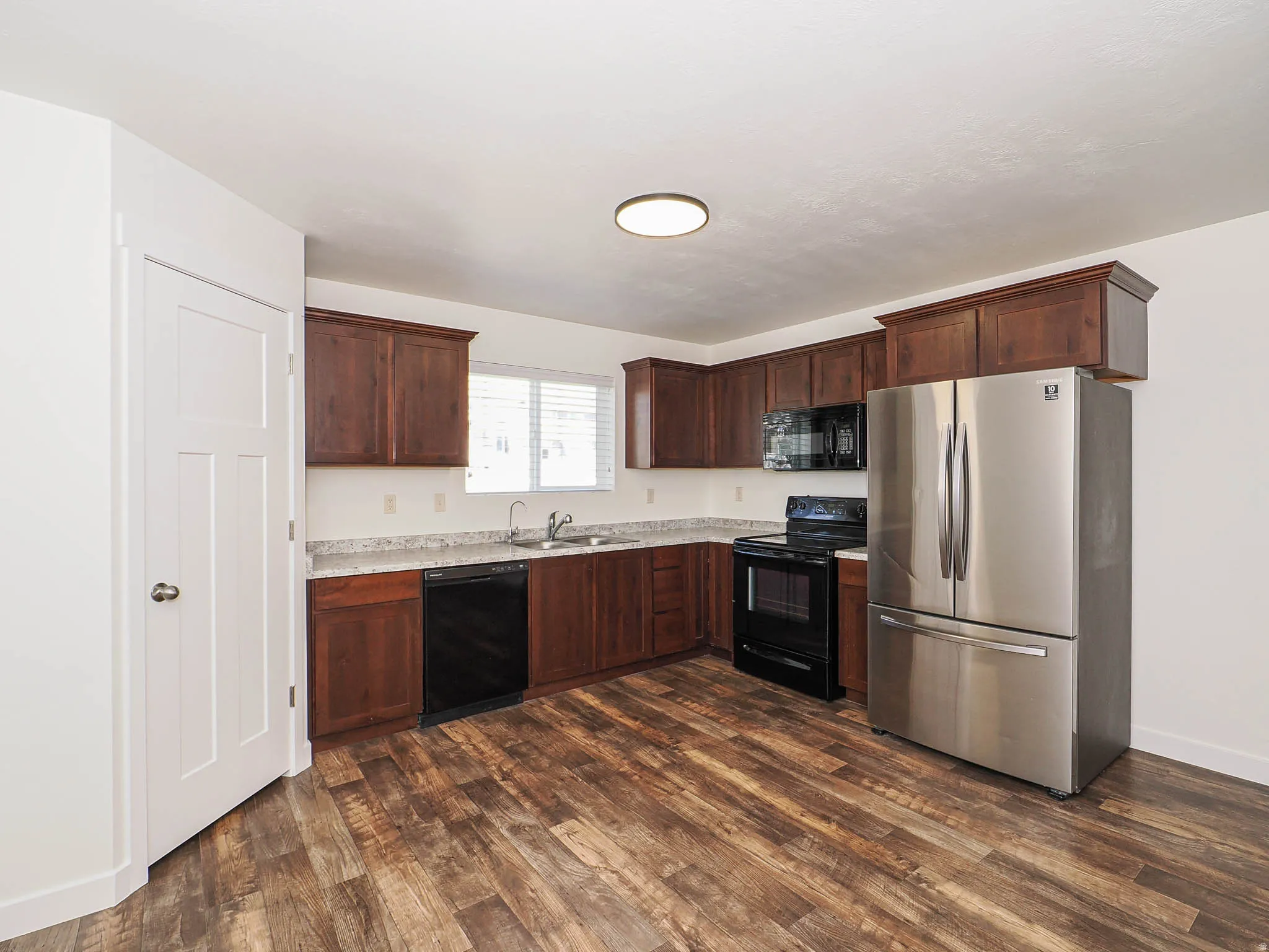 Kitchen featuring wood-finish flooring, dark wood cabinetry, light-toned countertops, and a full suite of stainless steel appliances