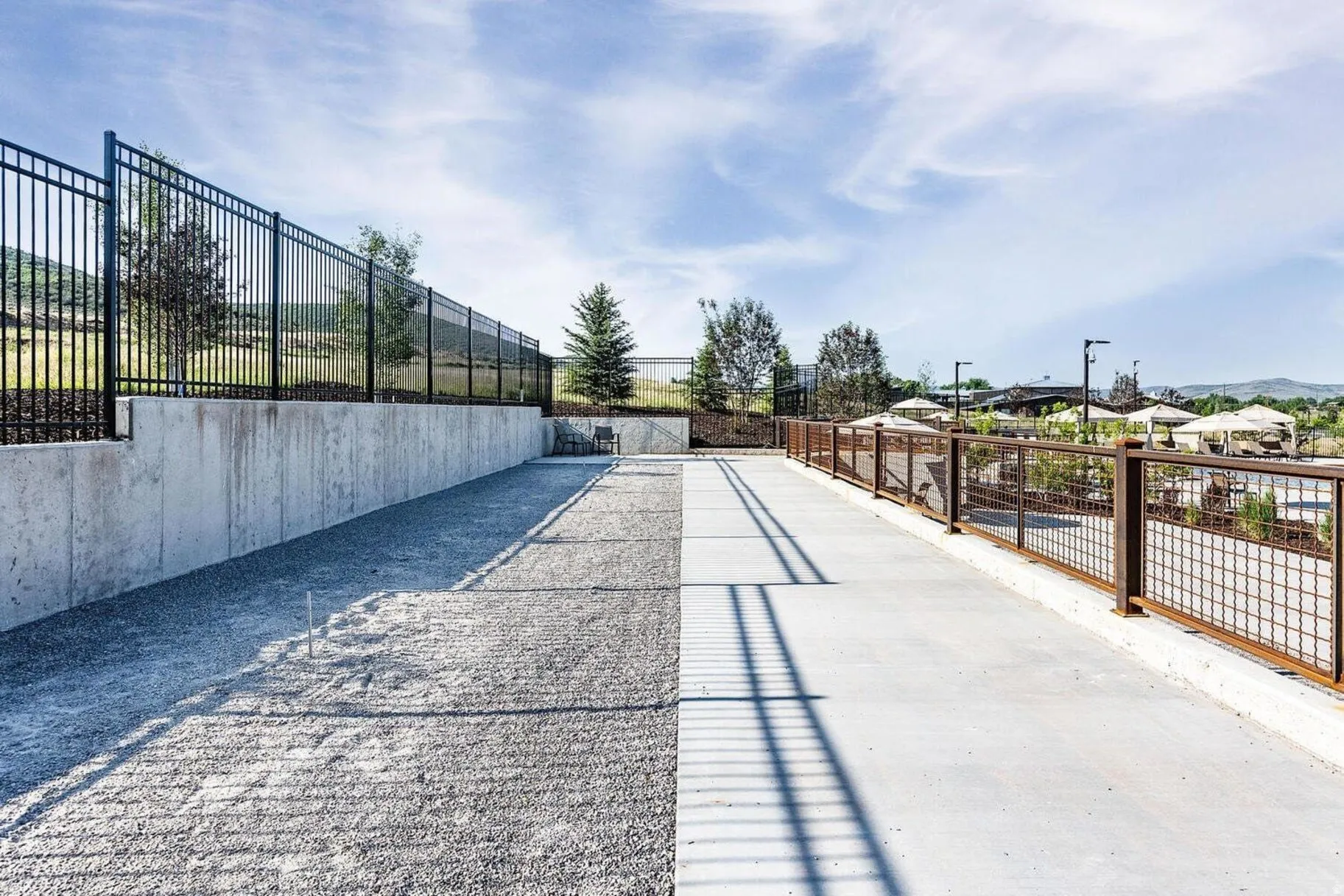 Outdoor concrete path bordered by a metal grid fence, with a gravel area to the left